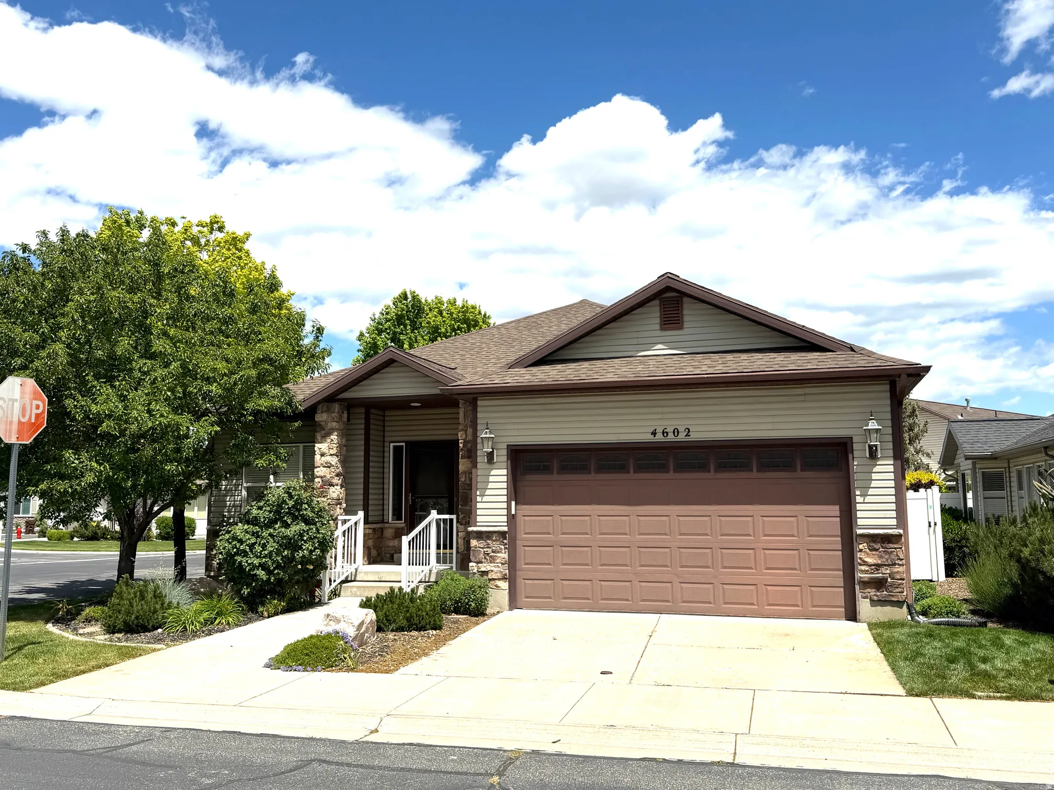 Single-story residence featuring a two-car garage with a brown panel door, light beige siding, and stone accents
