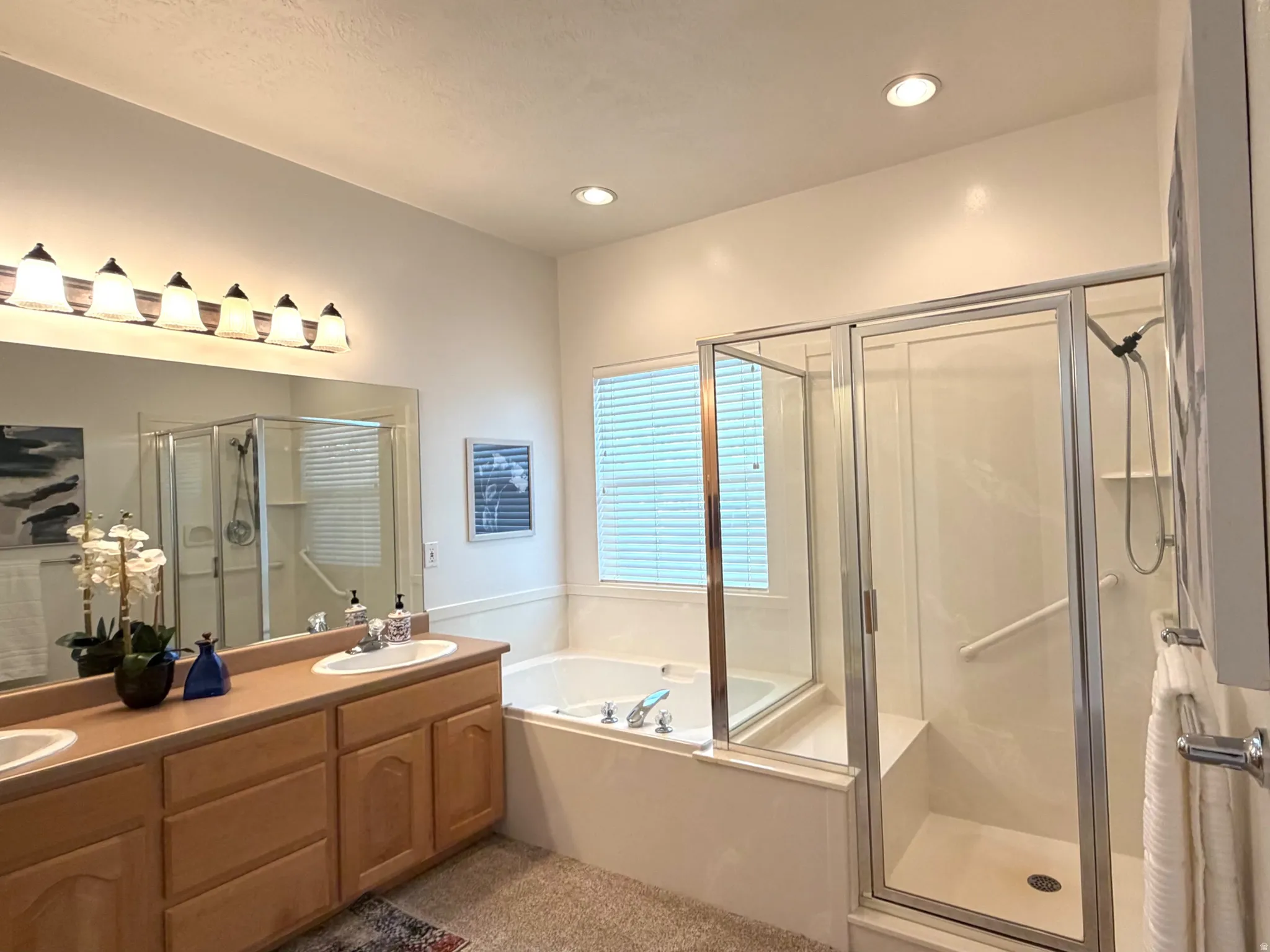 Bathroom featuring a dual vanity with wood cabinetry, a built-in jetted tub, and a separate glass-enclosed shower with a bench