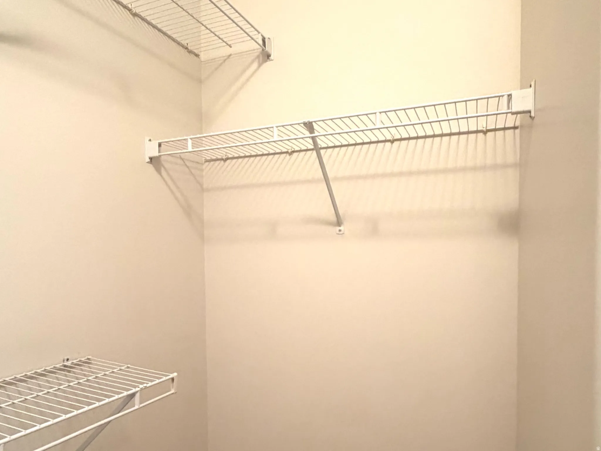 Walk-in closet with multiple white wire shelving units and light beige carpeting