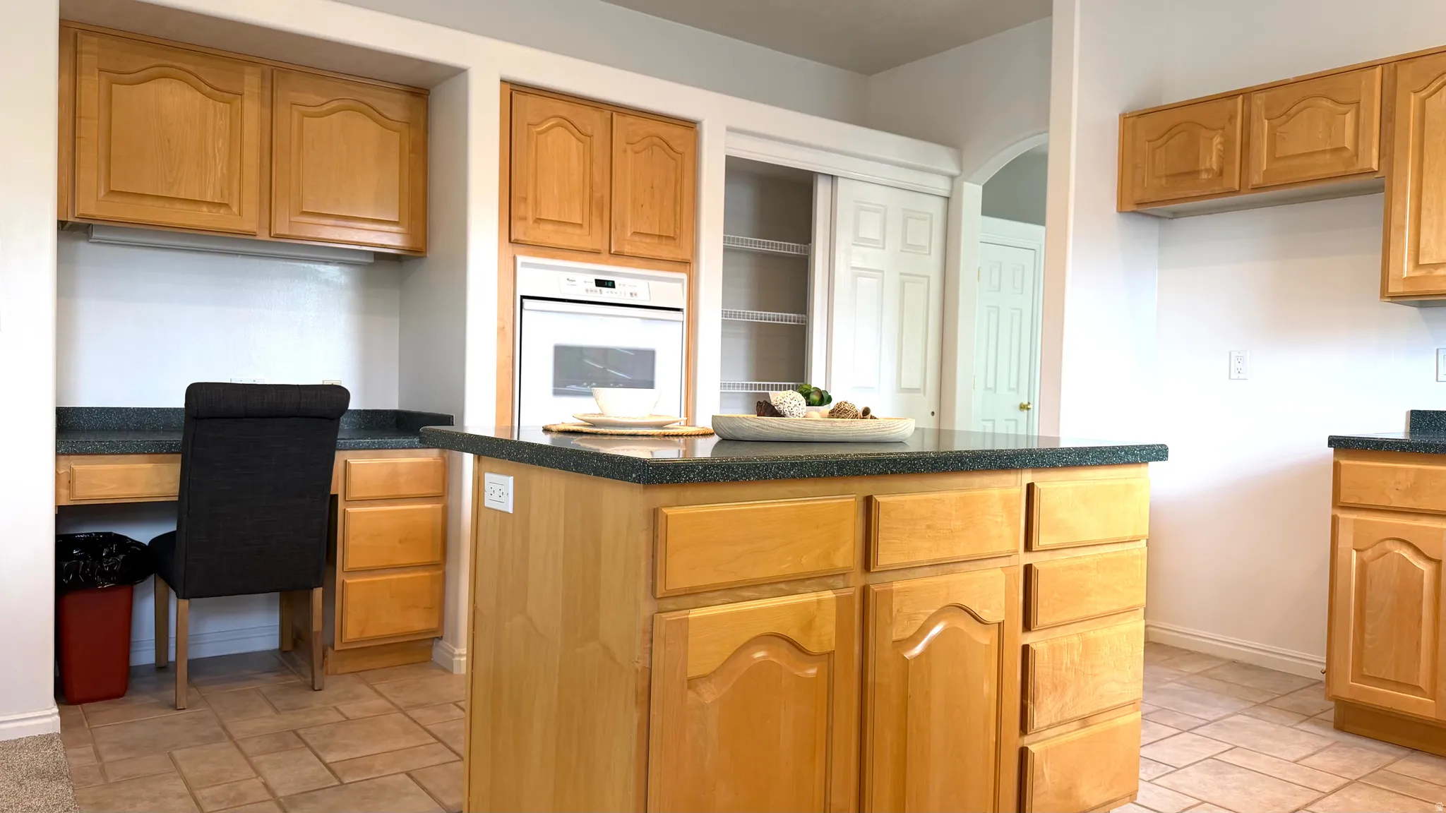 Kitchen featuring a central island with countertop, wood-finish cabinetry, integrated built-in oven, and a dedicated desk area with upper storage