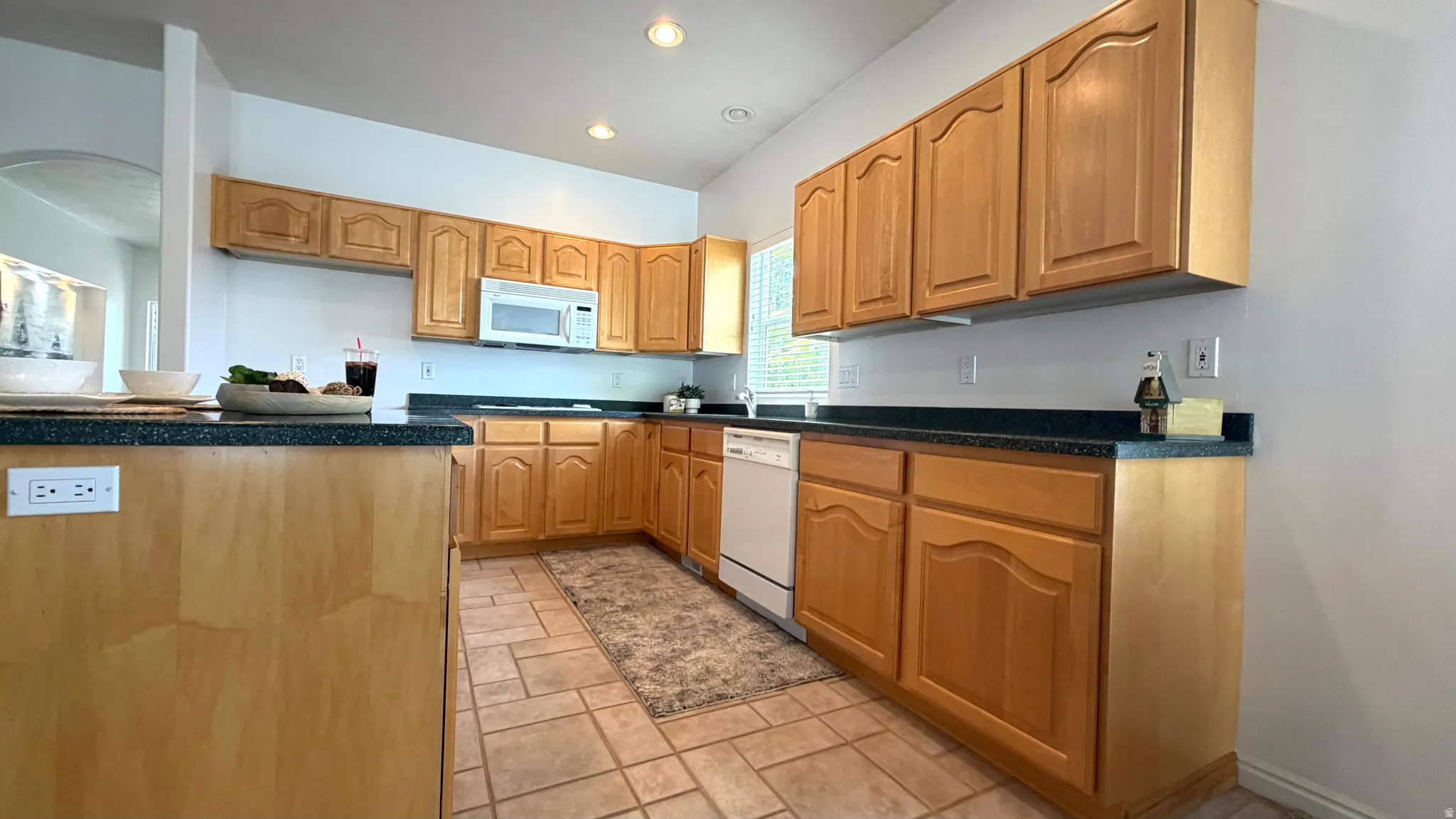 Kitchen featuring wood-finish cabinetry, dark countertops, a built-in microwave, and a white dishwasher