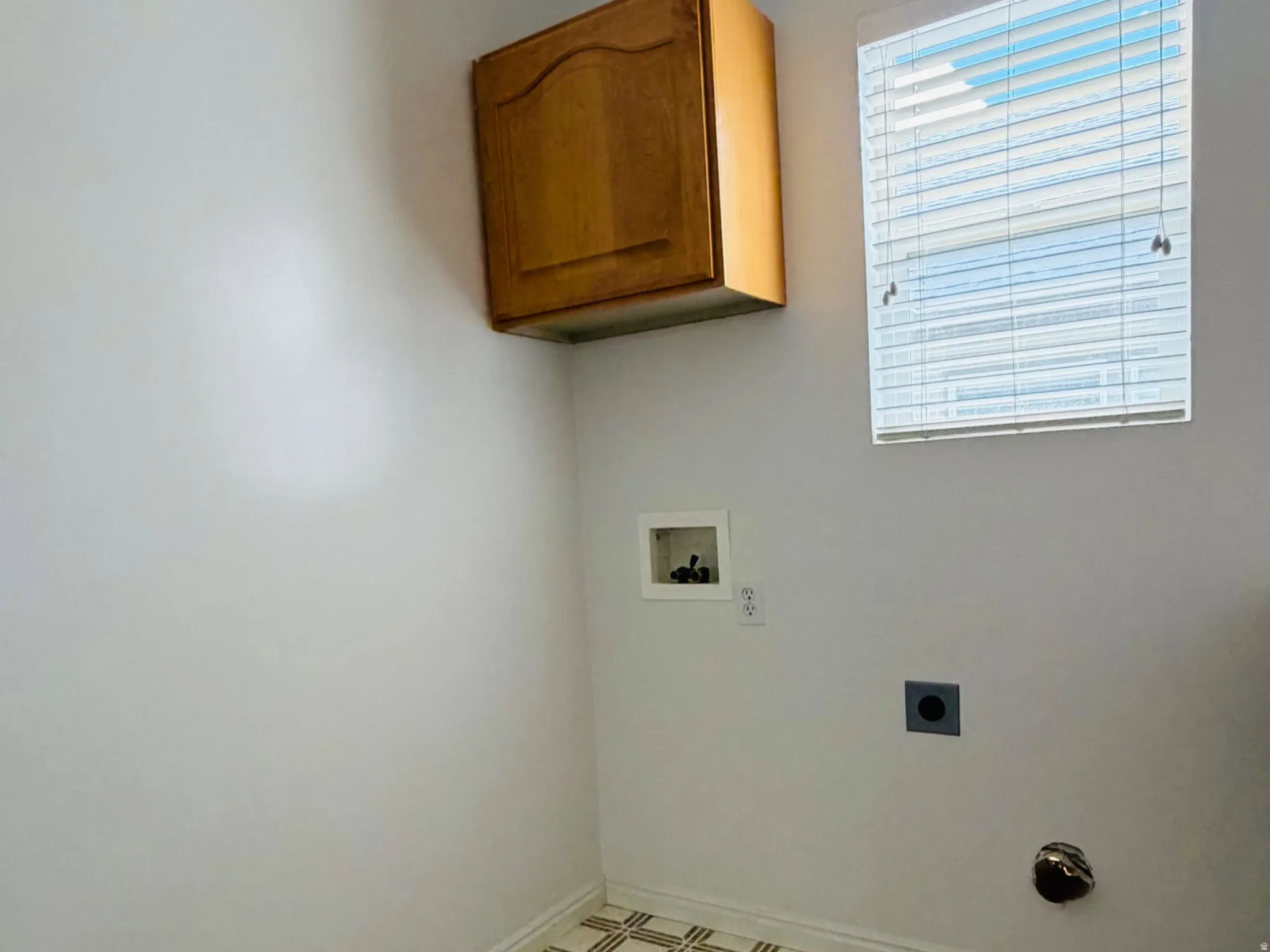 Utility space featuring patterned flooring, a window with horizontal blinds, and a wall-mounted wooden cabinet