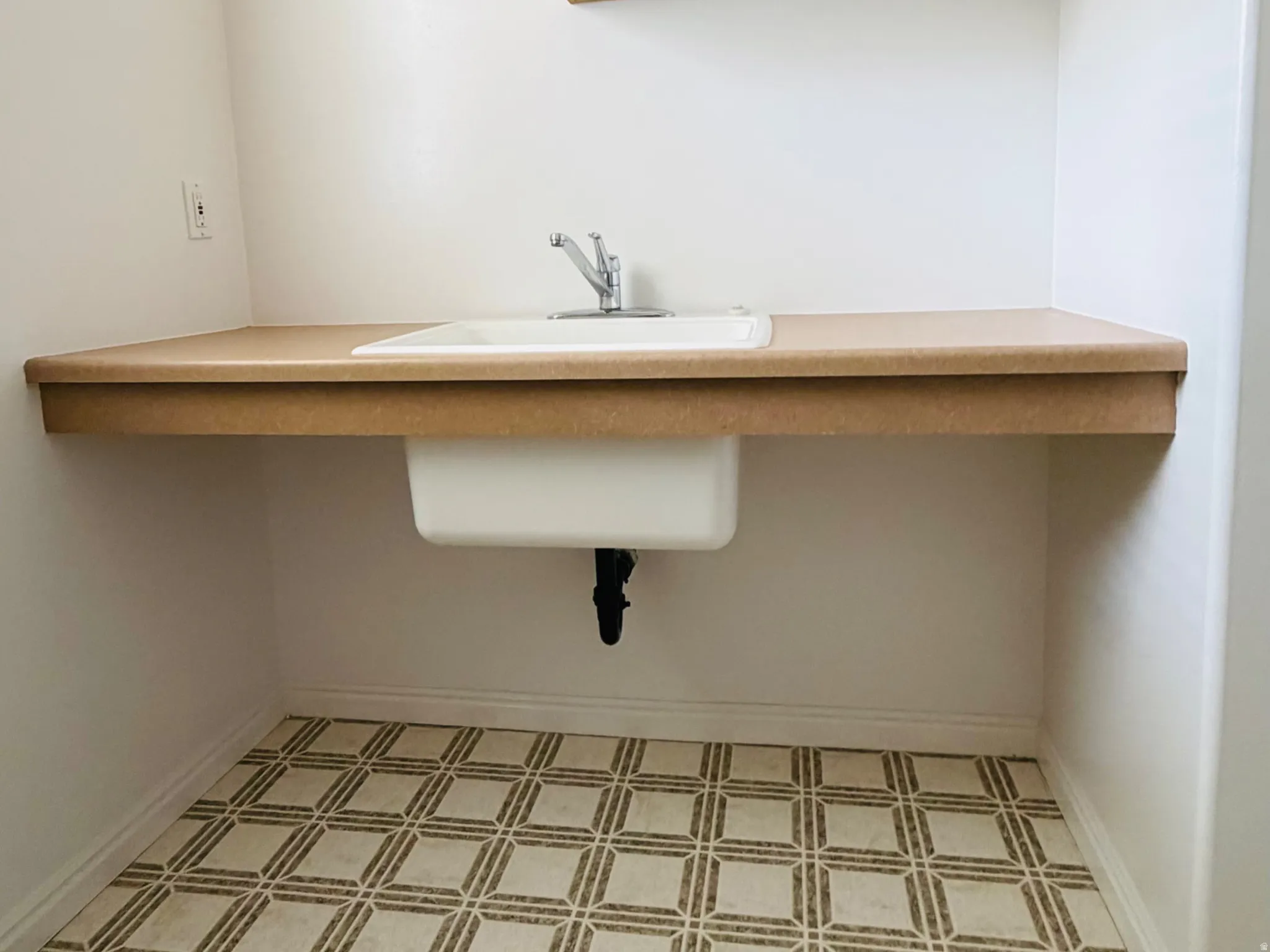 Utility area featuring a wall-mounted sink with countertop space, natural wood-finish cabinetry, and patterned floor tiling