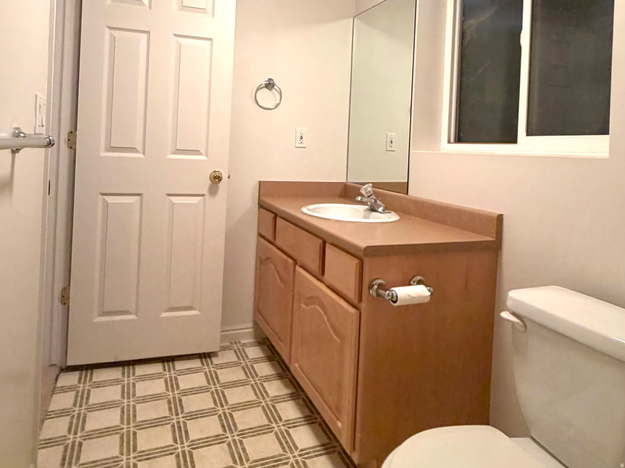Bathroom featuring a light wood-finish vanity with a built-in sink, a wall-mounted mirror, patterned tile flooring, and a window providing natural light
