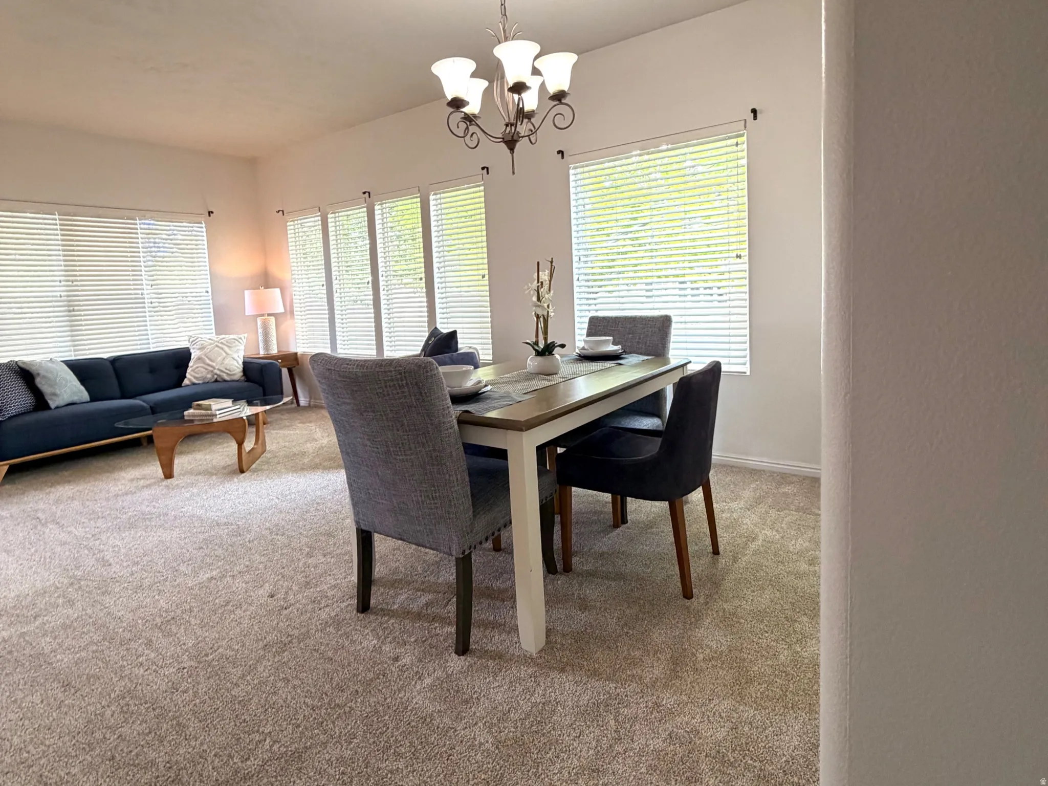 Formal dining space featuring a bronze chandelier with frosted glass shades, multiple windows, and light-colored carpeting