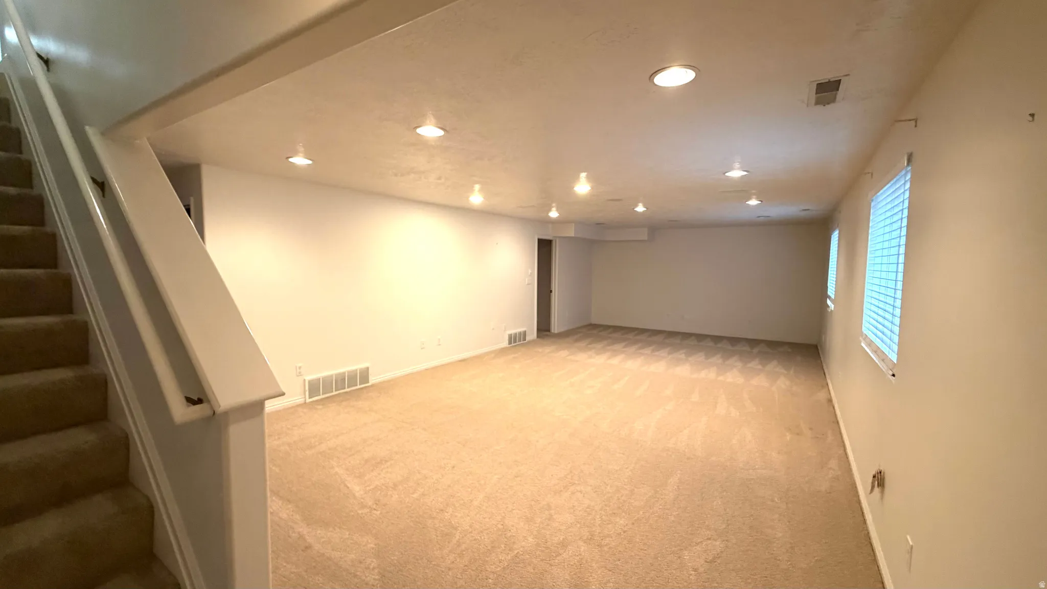 Spacious carpeted room featuring recessed lighting, multiple windows with blinds, and a neutral color palette