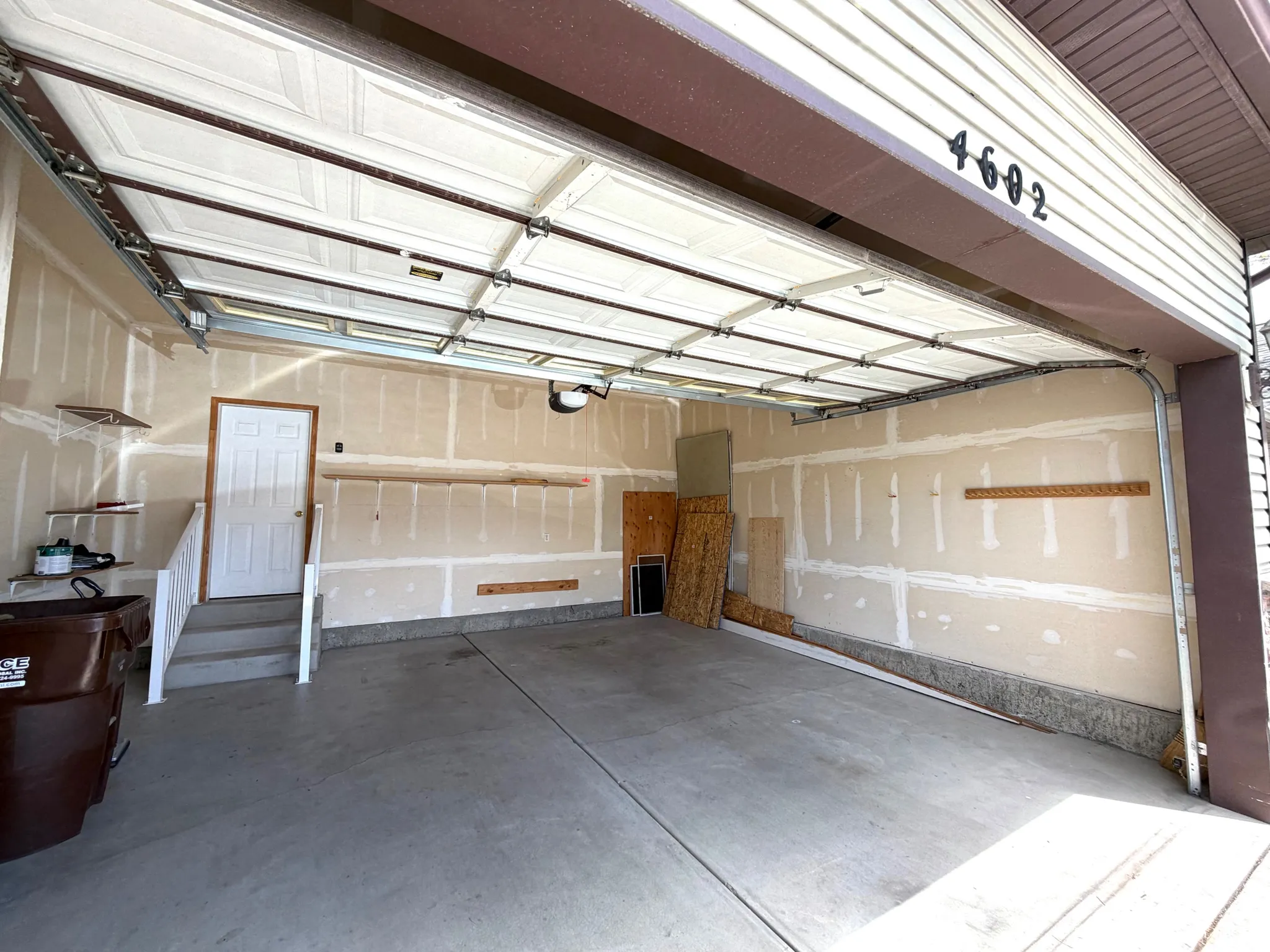 Spacious attached garage featuring a concrete floor, an overhead garage door, built-in shelving, and a pedestrian access door