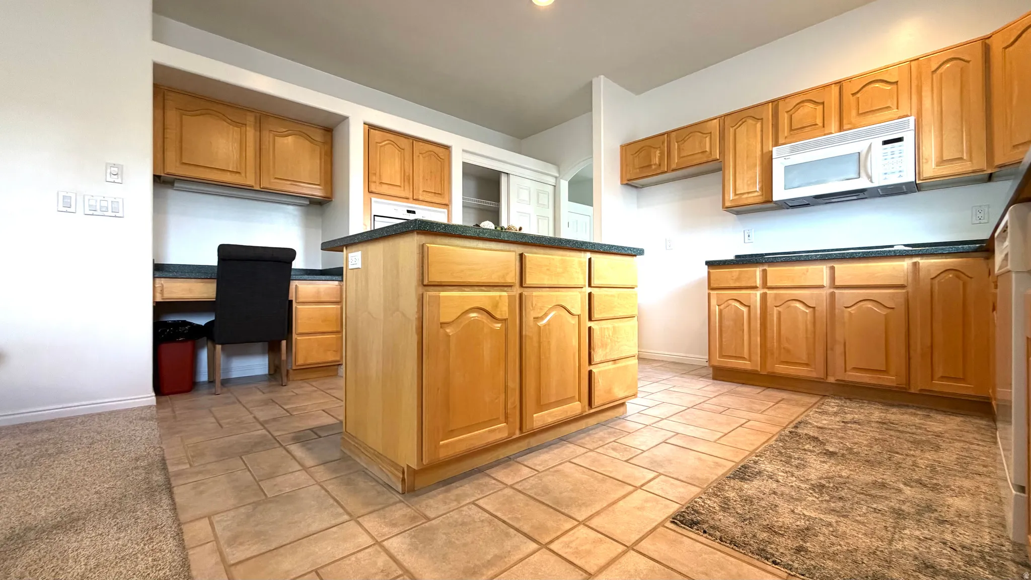 Kitchen featuring a central island, light wood cabinetry, stone-look countertops, a built-in microwave, and tile flooring
