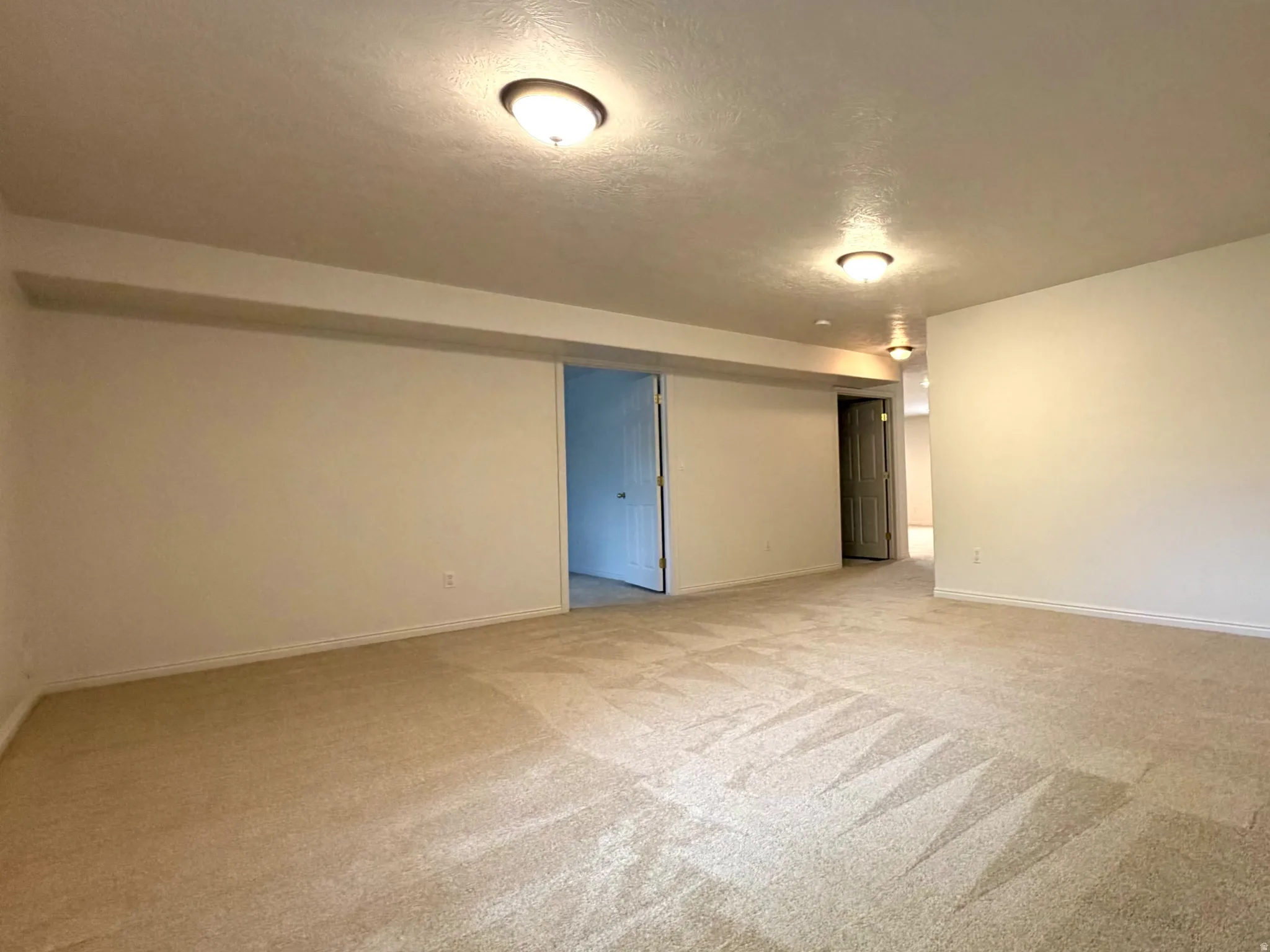 Spacious room featuring neutral carpeting, light-toned walls, recessed lighting, and a doorway