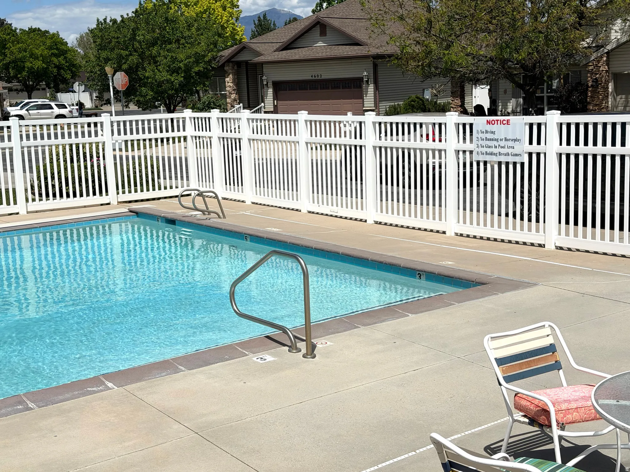 Subject home in background. Outdoor swimming pool featuring a white privacy fence, light-colored concrete deck, and two stainless steel pool handrails
