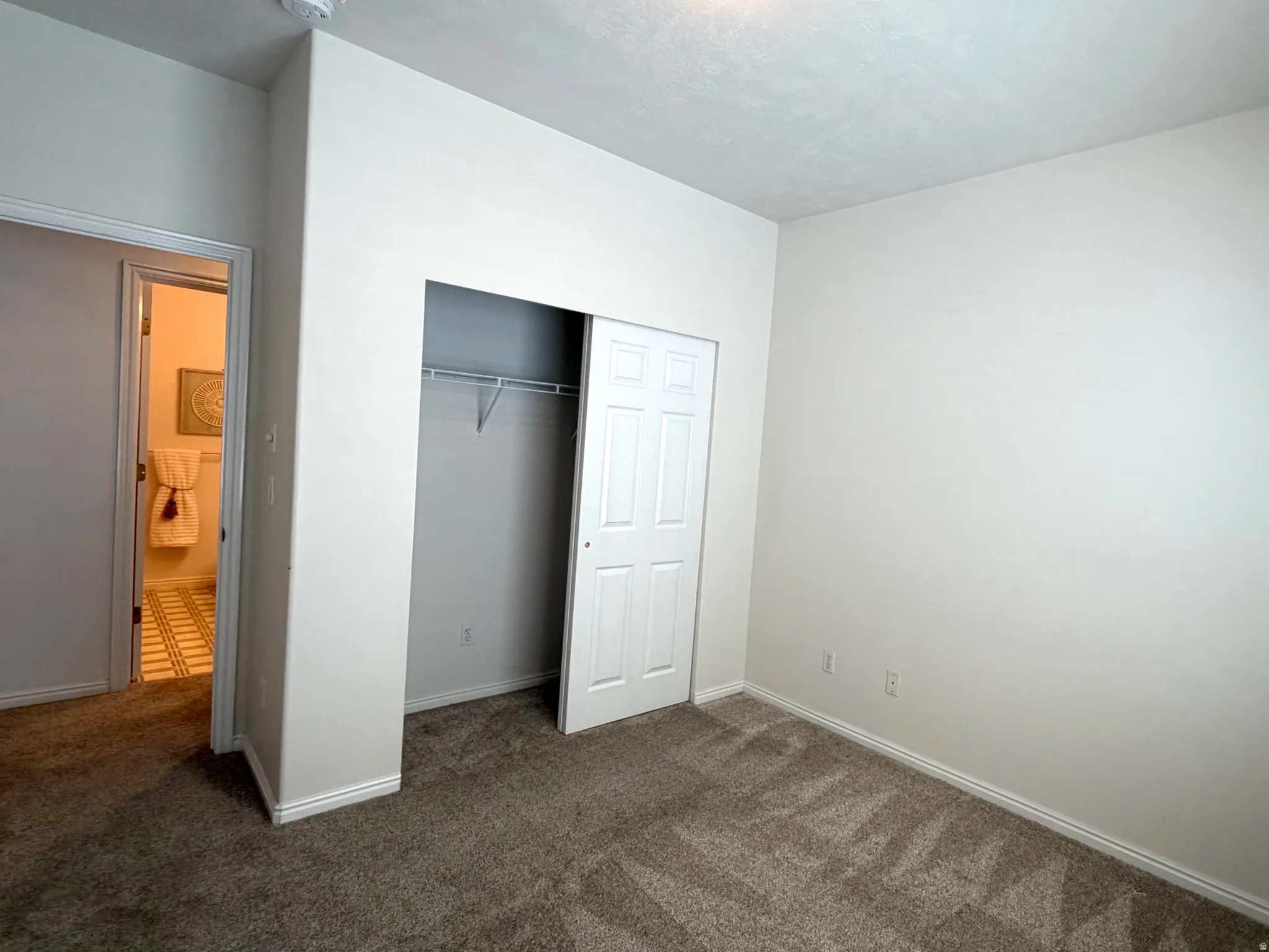 Neutral-toned interior room featuring textured carpeting, white baseboards, and a bi-fold closet with an interior wire shelf