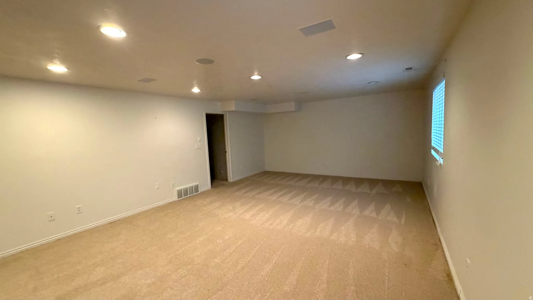 Spacious room featuring neutral carpet flooring, recessed lighting, and a single window with horizontal blinds