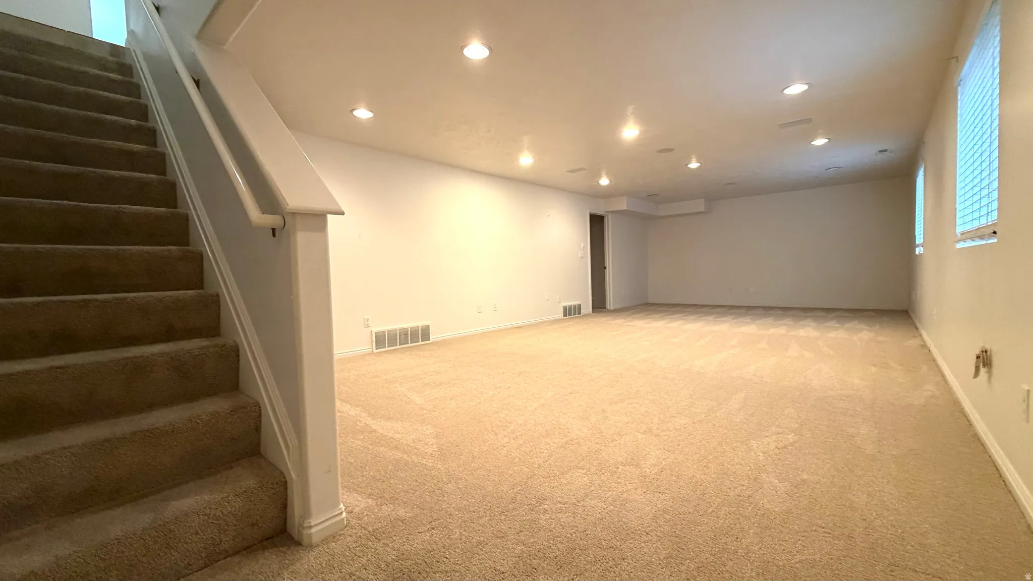 Spacious carpeted room featuring recessed lighting and a built-in staircase with a painted wood handrail