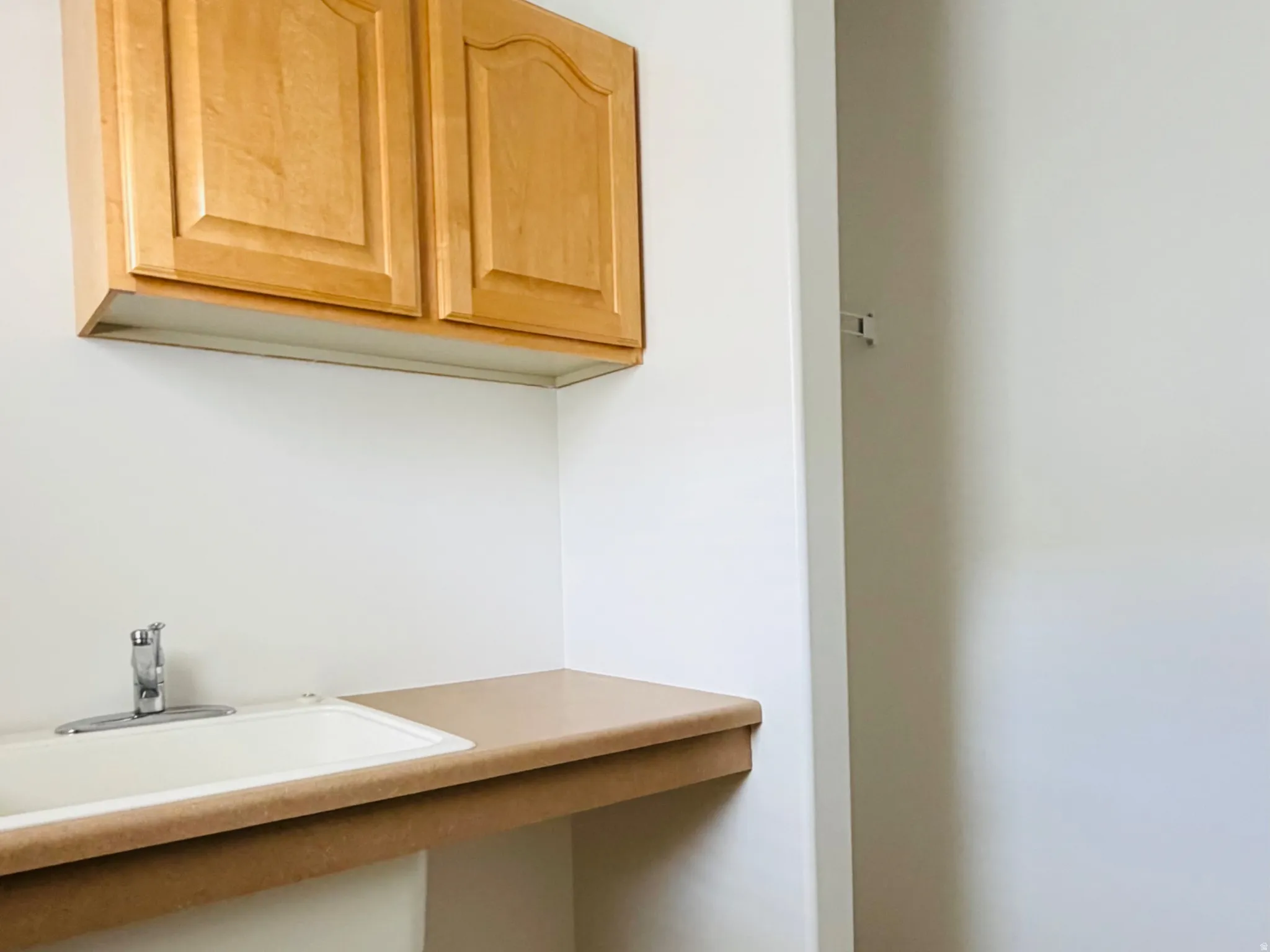 Utility room featuring a utility sink, light wood-finish cabinetry, and a patterned floor