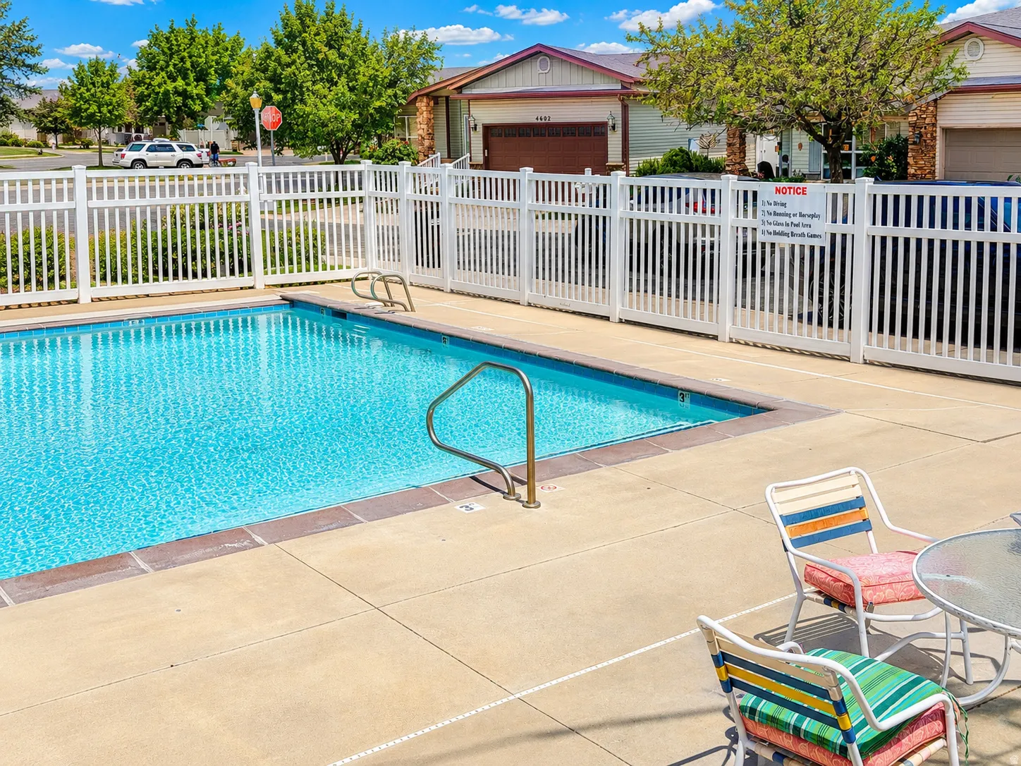 Sparkling outdoor pool featuring a concrete surround, white picket fencing, and stainless steel handrails