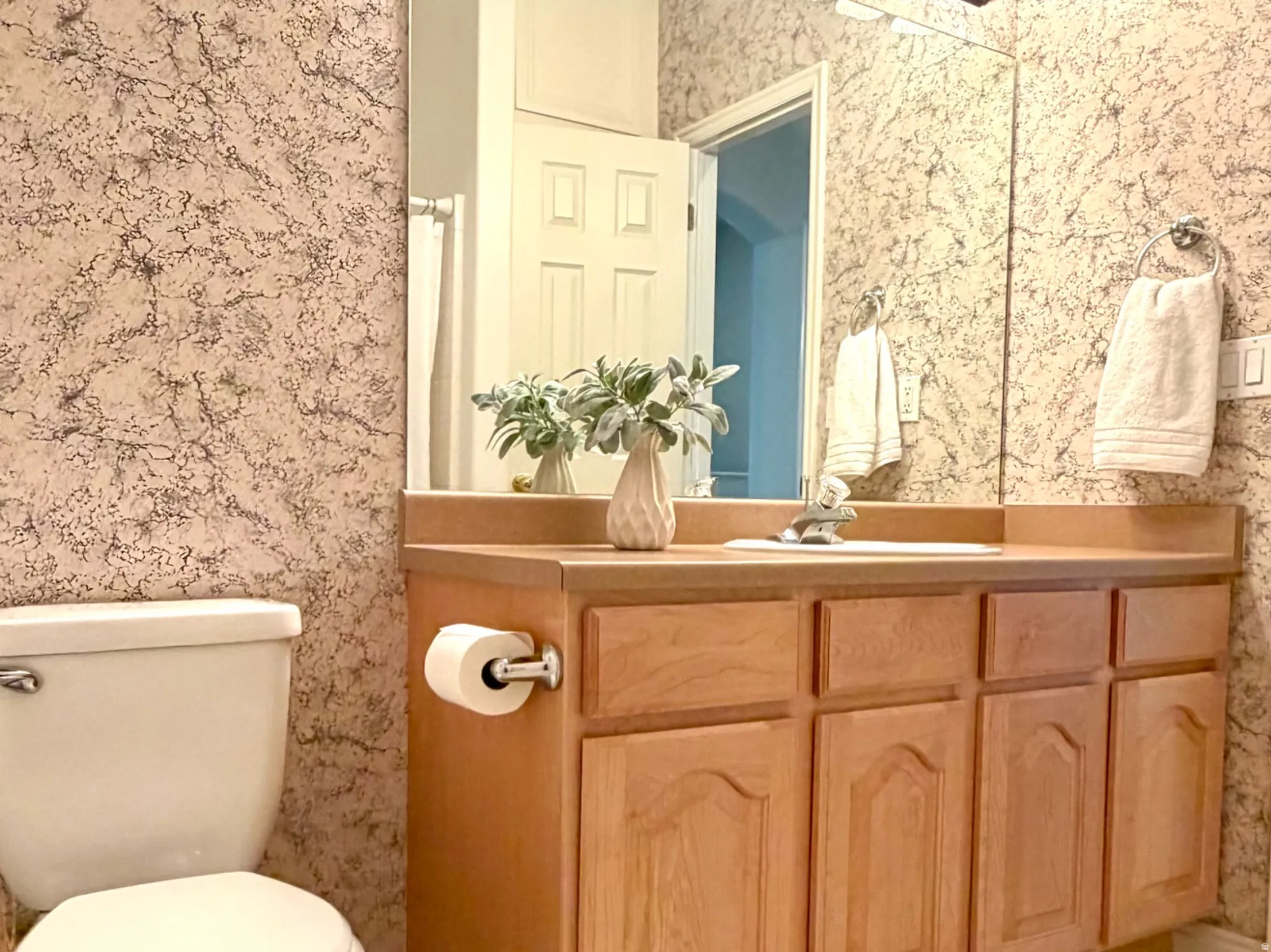 Bathroom featuring a wood-finish vanity with an integrated sink, patterned floor tiles, a wall-mounted mirror, and a multi-bulb vanity light fixture