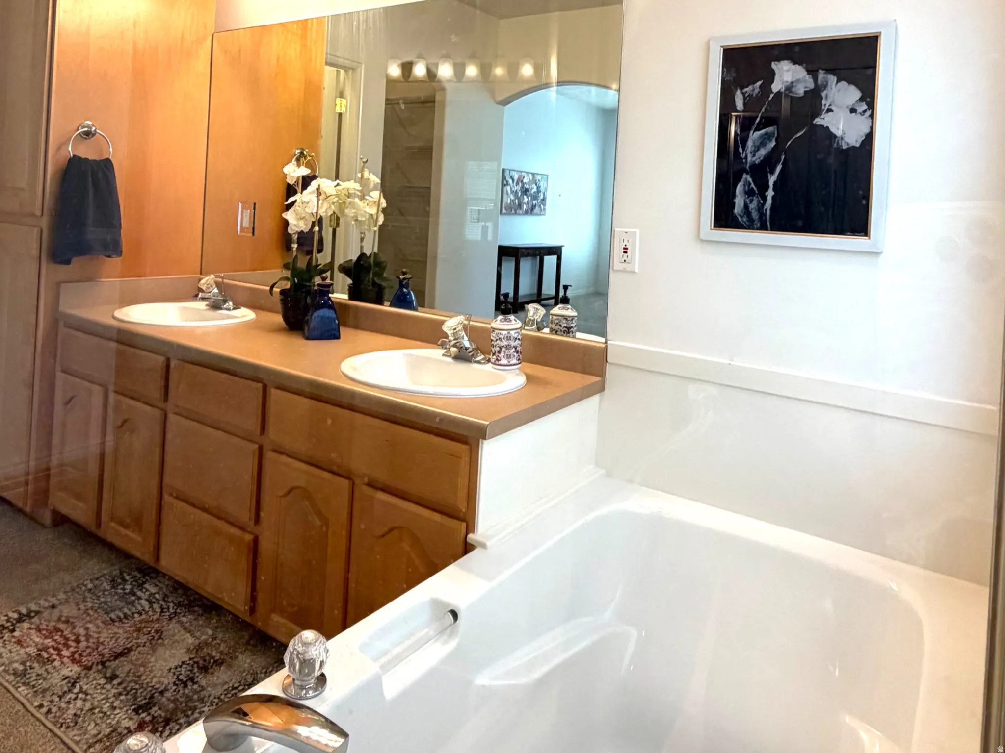 Spacious bathroom featuring a built-in soaking tub with clear knob fixtures, a dual sink vanity with oak-finish cabinetry, and a full-width mirror