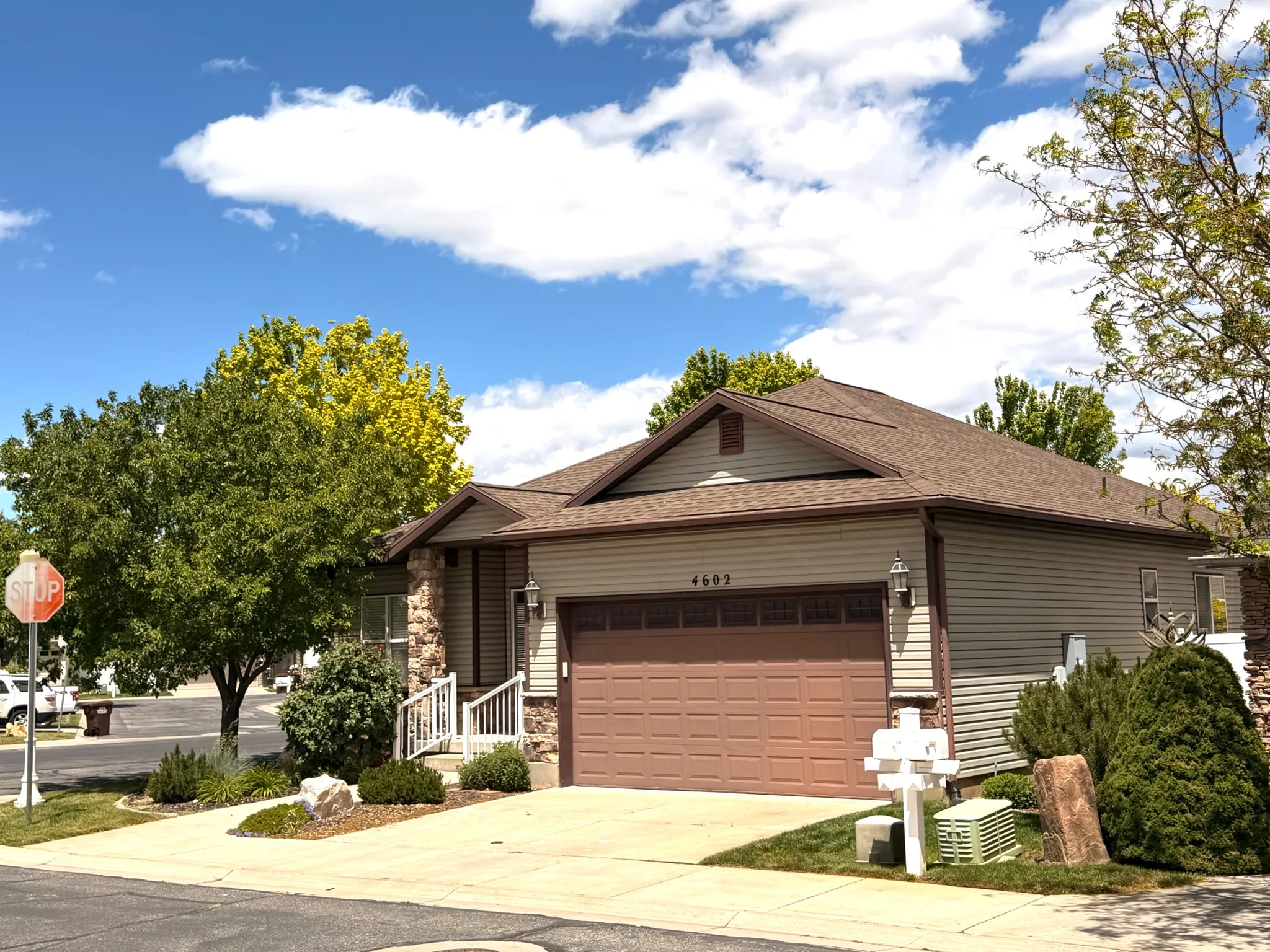 Single-story residence featuring light beige siding, a brown composition shingle roof, and a prominent two-car garage with a brown door