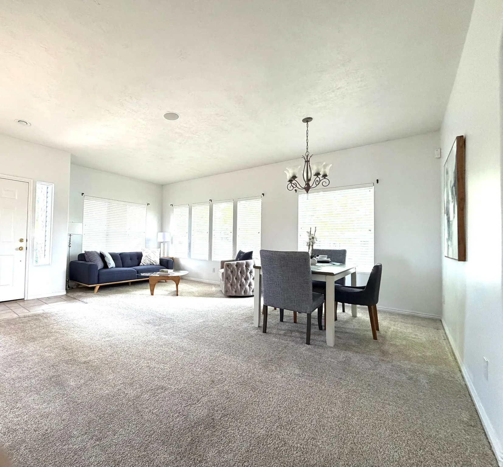 Spacious main living area featuring light-toned carpet flooring and multiple windows with blinds