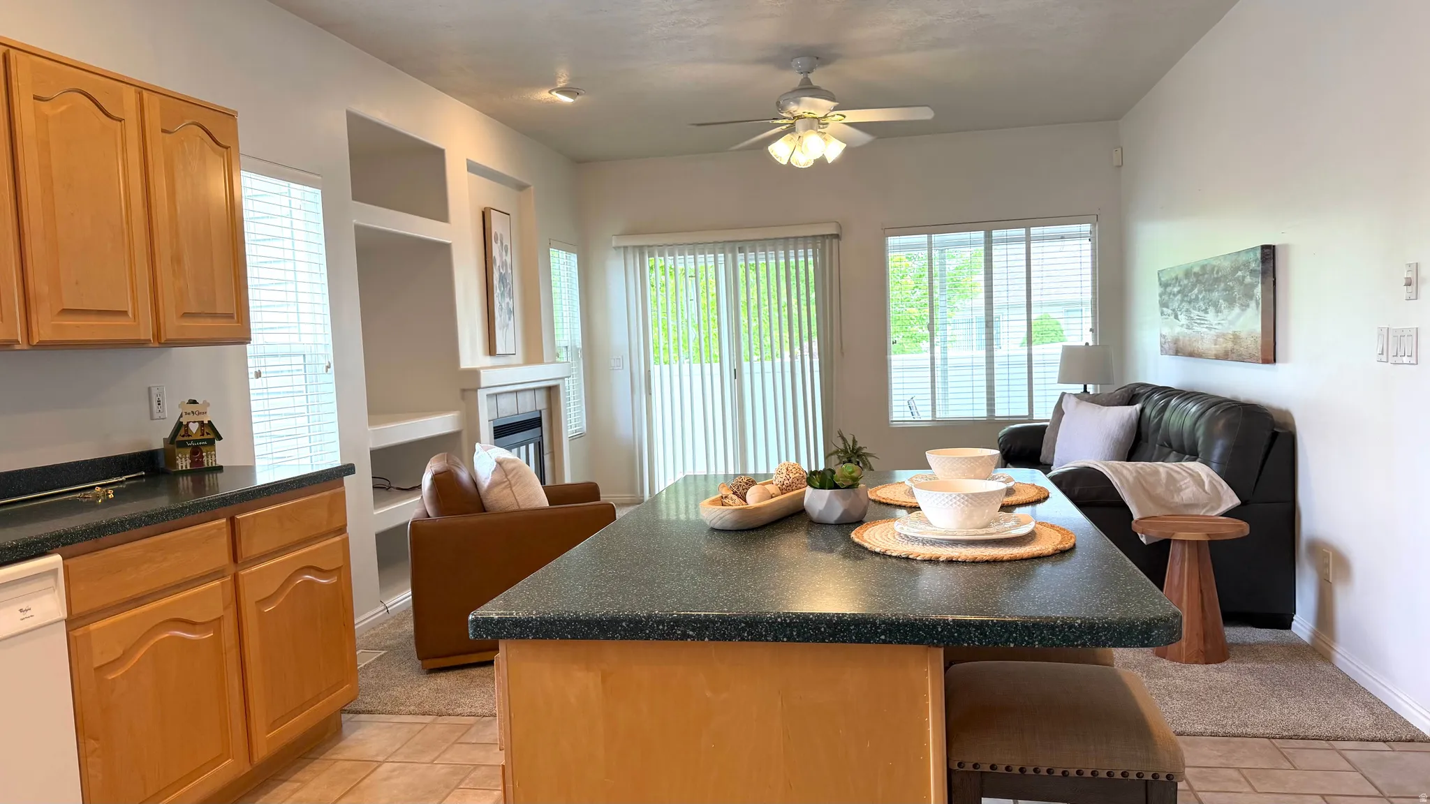 Open-concept living area featuring an eat-at kitchen island with a dark countertop, a fireplace with integrated shelving, and glass sliding doors leading to the exterior