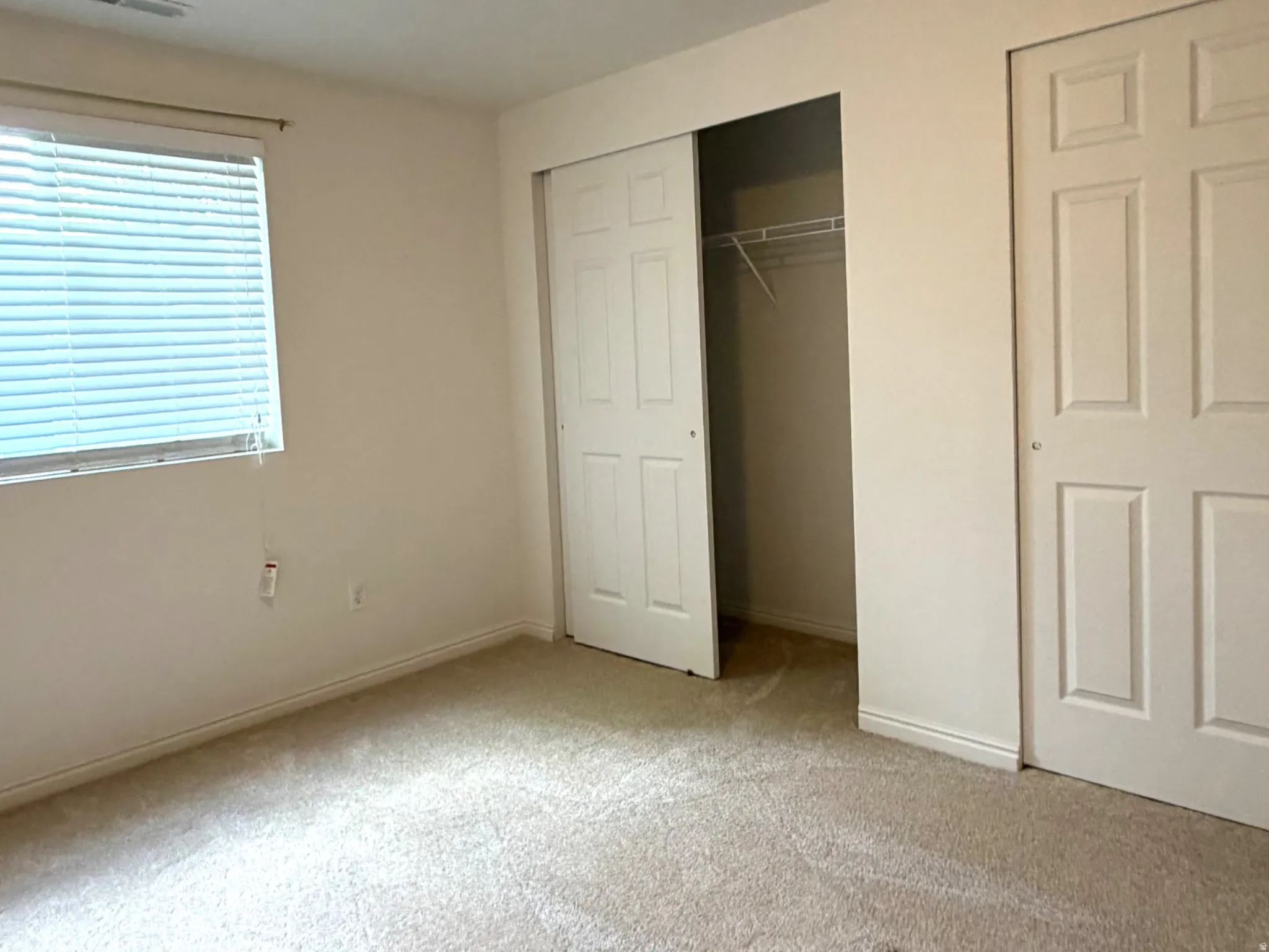 Carpeted room featuring a ceiling-mounted light fixture, a window with horizontal blinds, and a closet with bi-fold doors and built-in shelving