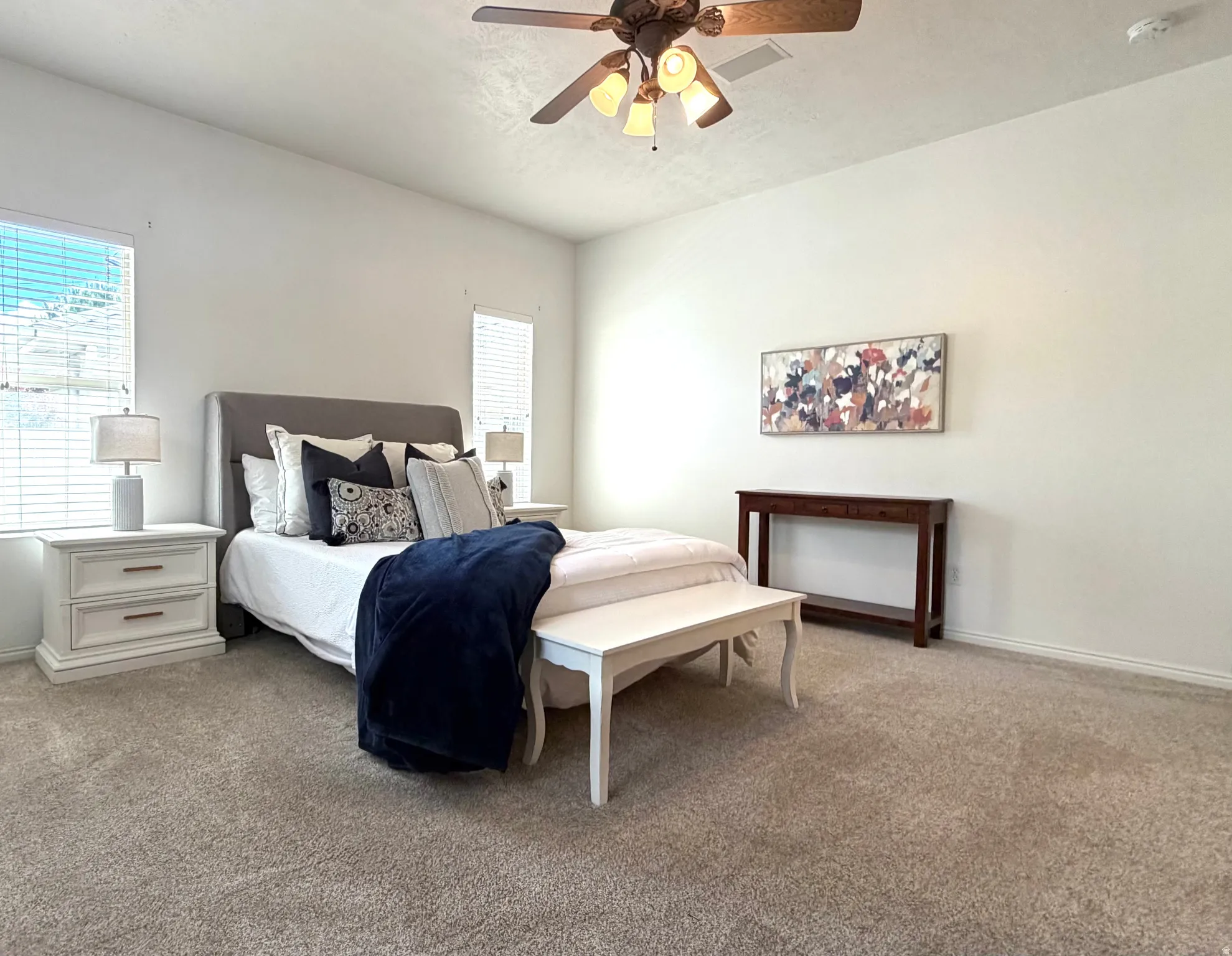 Spacious carpeted room featuring a ceiling fan with integrated lighting, multiple windows with horizontal blinds, and neutral wall tones