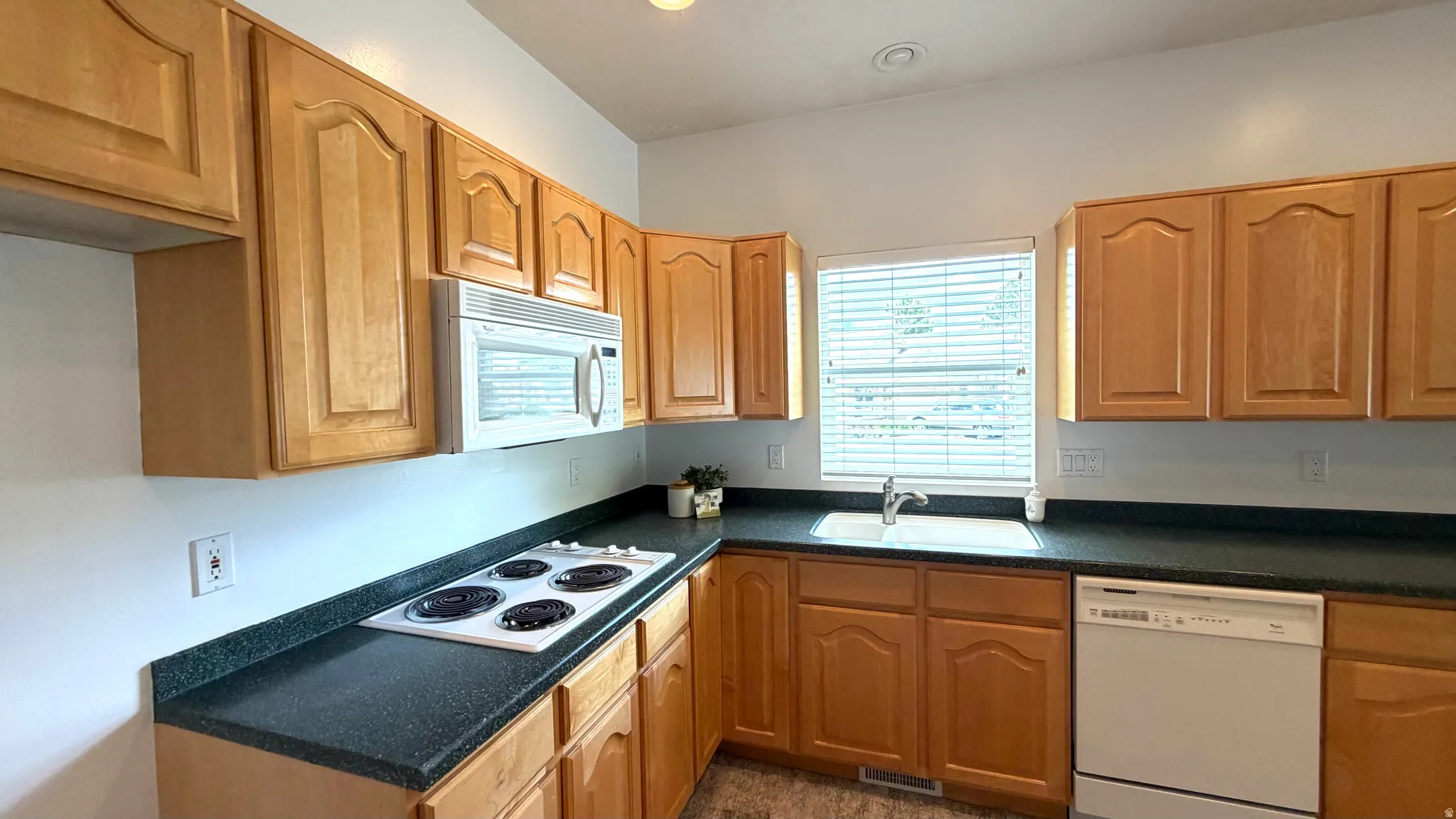 Kitchen featuring wood cabinetry, dark speckled countertops, a built-in microwave, an integrated sink, and an electric cooktop