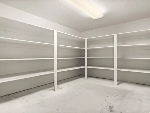 Spacious utility room featuring extensive built-in white shelving, a neutral concrete floor, and overhead fluorescent lighting