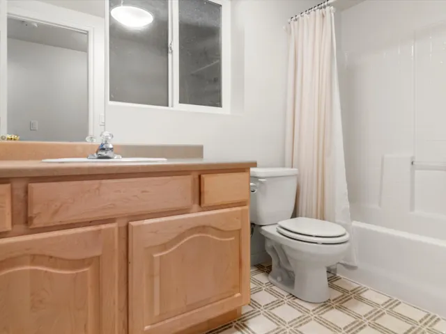 Bathroom featuring a light wood-finish vanity with an integrated sink, patterned floor tiling, and a white bathtub with tile surround