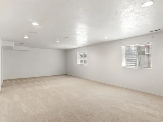 Spacious interior room featuring light-toned carpeting, white walls, and recessed lighting