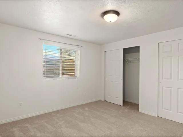 Carpeted room featuring a single window with blinds, white walls, and a ceiling-mounted light fixture