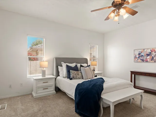 Carpeted room featuring two windows with blinds, a ceiling fan with integrated lighting, and white walls