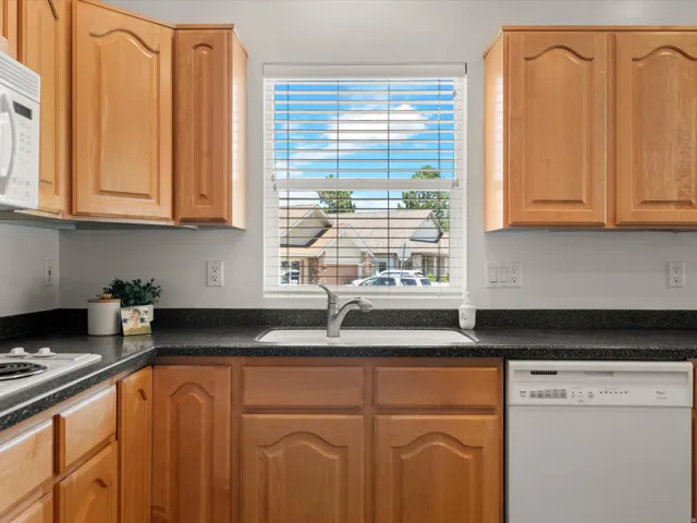 Kitchen featuring light wood cabinetry, a dark countertop, an integrated sink with a stainless steel faucet, and a window with horizontal blinds