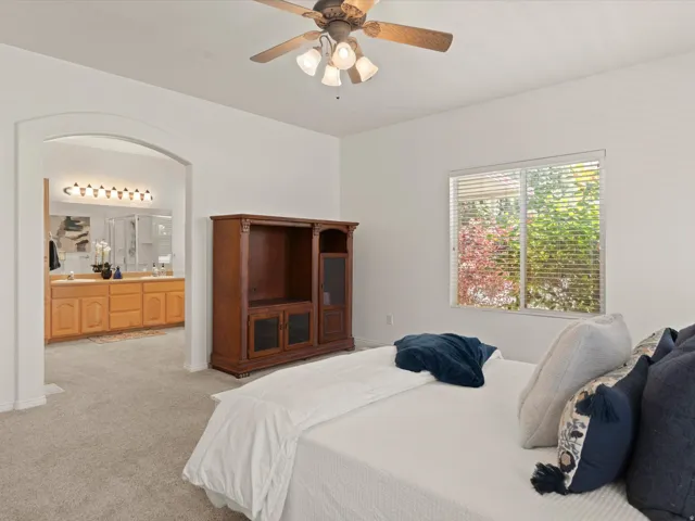 Carpeted bedroom featuring an arched doorway, ceiling fan with light kit, and a window with horizontal blinds