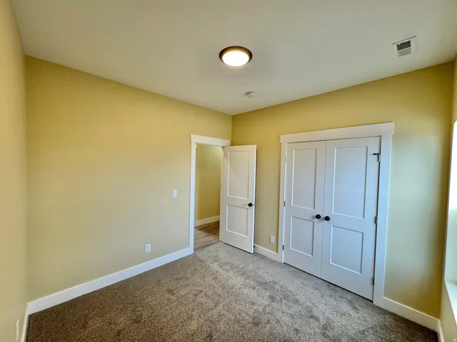 Carpeted room featuring a ceiling-mounted light fixture, white trim, and a double-door closet with dark hardware