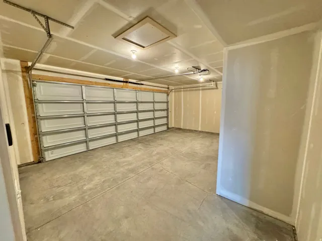 Spacious garage with concrete flooring, automatic garage door opener, and multiple overhead light fixtures