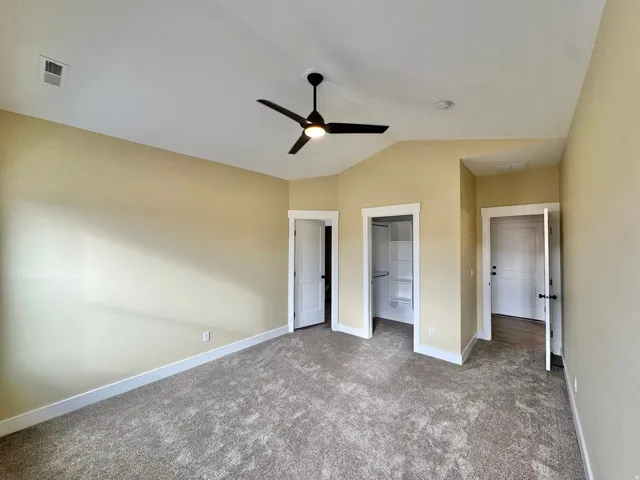 Carpeted room featuring a ceiling fan with light, vaulted ceiling, and built-in closet shelving