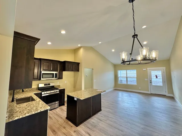 Open-concept kitchen and living area featuring dark wood-finish cabinetry, light-toned countertops, and stainless steel appliances