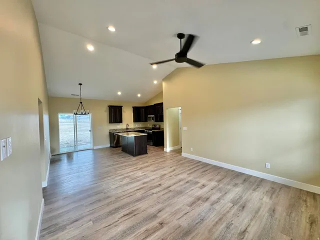 Open-concept living space featuring wood-finish flooring, vaulted ceilings with recessed lighting, and a modern ceiling fan