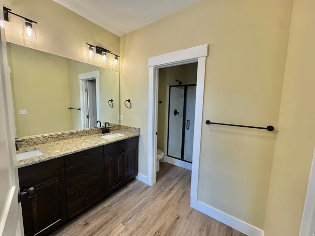 Dual vanity with granite-finish countertop, dark wood-finish cabinetry, and matte black fixtures