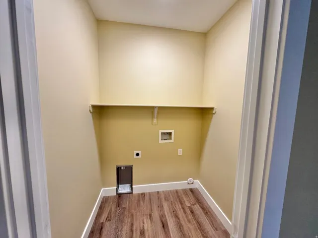 Dedicated utility room featuring wood-finish flooring, light-colored walls, white baseboards, and an integrated wall shelf