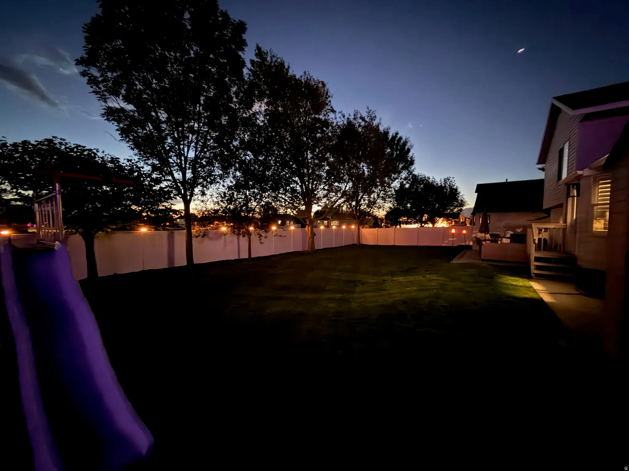 Expansive backyard featuring a manicured lawn, full privacy fencing, and mature trees