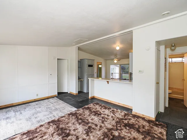 Open-concept living area featuring a breakfast bar, gray cabinetry, white walls with wood trim, and dark flooring