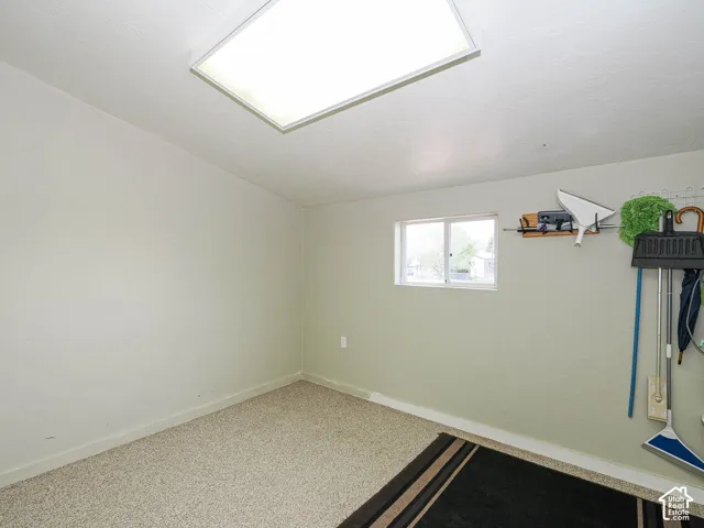 Flush-mount ceiling light fixture illuminates this room featuring light-colored carpet, a single window, and painted walls