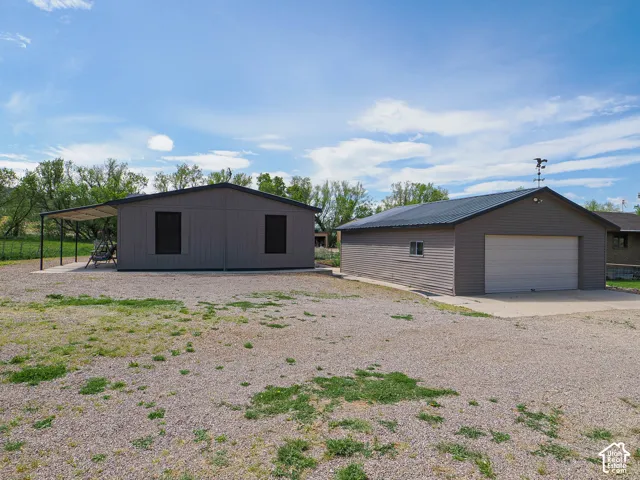 Property featuring two detached structures: a gray outbuilding with a covered patio area and a separate garage building with a concrete drive