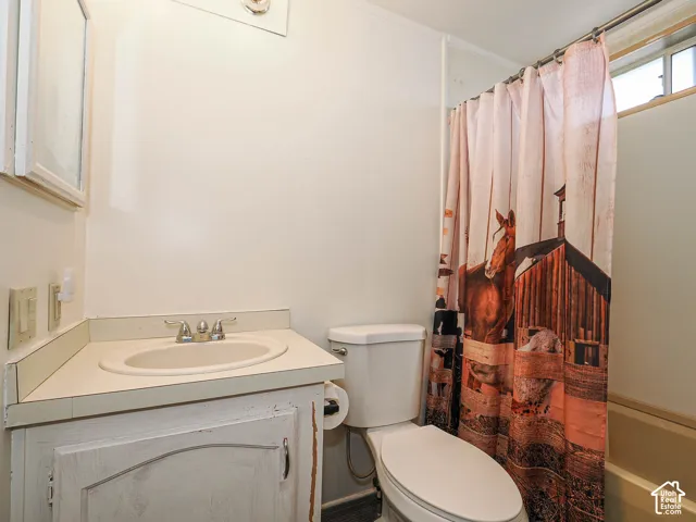 Bathroom featuring a single vanity with an integrated sink, chrome faucet, toilet, and a bathtub with an overhead window