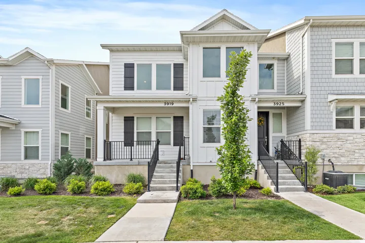 Modern townhome exterior featuring light-toned siding, dark shutters, and a covered porch