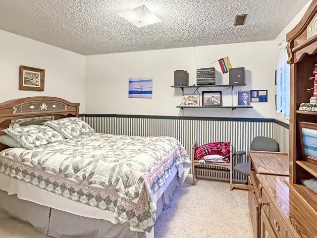 Bedroom featuring a wood-finish headboard, wall-mounted shelving, and striped wall detailing