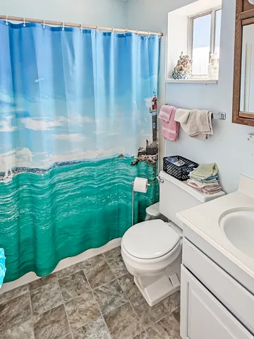 Bathroom featuring a white toilet, light gray vanity with a single sink, wood-finish framed mirror, and a frosted glass window