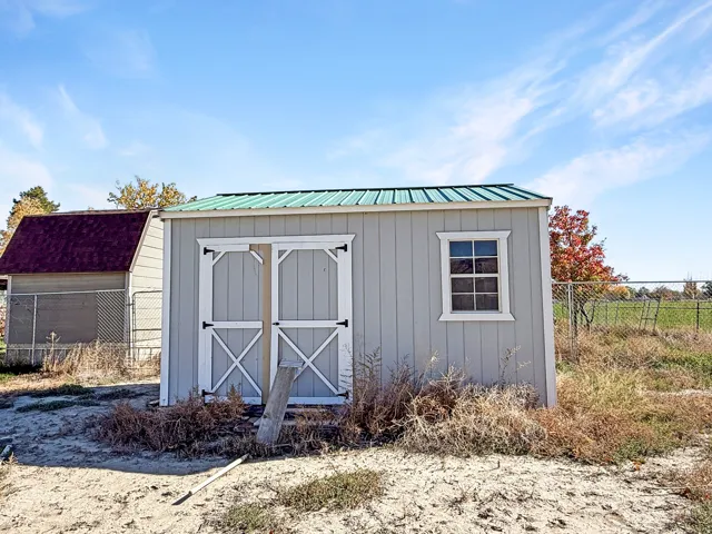 Light gray utility shed featuring a green metal roof, double barn doors with white trim, and a single-pane window